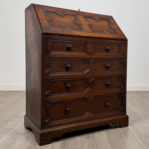 fig 8. A dark oak Jacobean style slant-front bureau featuring geometric inlaid panels and four drawer fronts with turned wooden knobs.