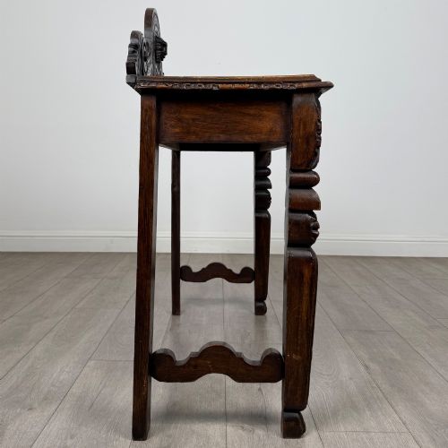fig 6. A dark carved oak Victorian side table featuring a sculpted mask upstand gallery, relief-carved frieze, and detailed carved legs.