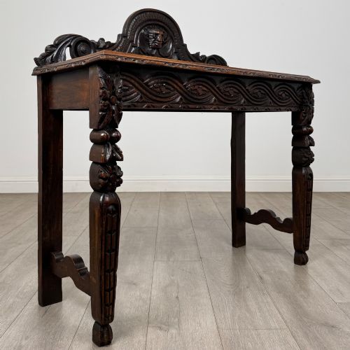 fig 7. A dark carved oak Victorian side table featuring a sculpted mask upstand gallery, relief-carved frieze, and detailed carved legs.