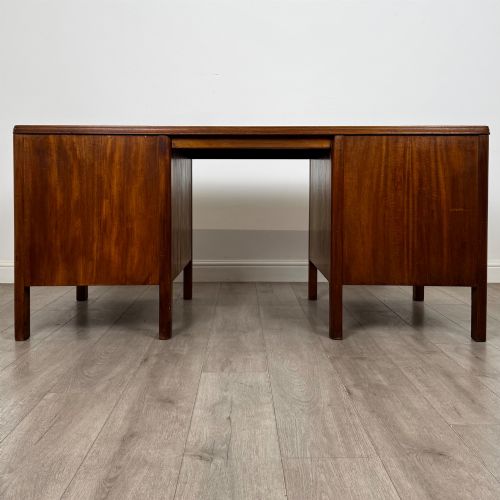 fig 4. A large mid-20th century mahogany pedestal desk featuring two sets of drawers with brass drop handles and a central kneehole.
