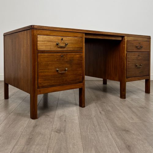 fig 7. A large mid-20th century mahogany pedestal desk featuring two sets of drawers with brass drop handles and a central kneehole.