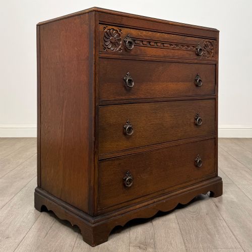fig 7. A dark oak chest of four drawers decorated with carved floral rosettes and dark metal drop ring handles.