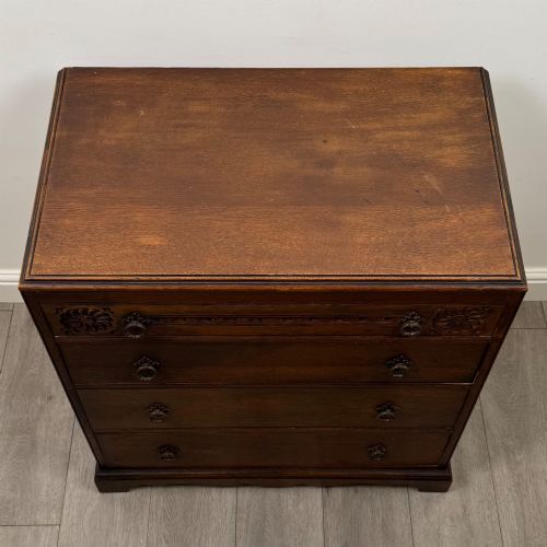 fig 8. A dark oak chest of four drawers decorated with carved floral rosettes and dark metal drop ring handles.