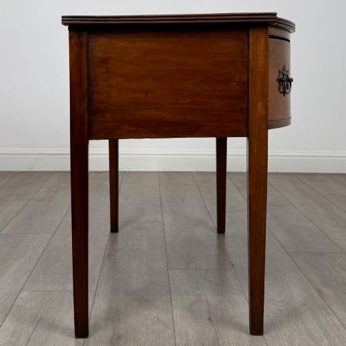 fig 6. An 18th-century Georgian mahogany writing table with a bow-front top, three drawers fitted with brass handles, supported by square tapered legs.