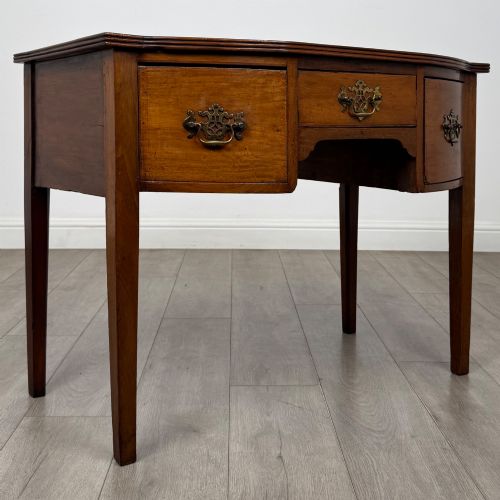 fig 7. An 18th-century Georgian mahogany writing table with a bow-front top, three drawers fitted with brass handles, supported by square tapered legs.