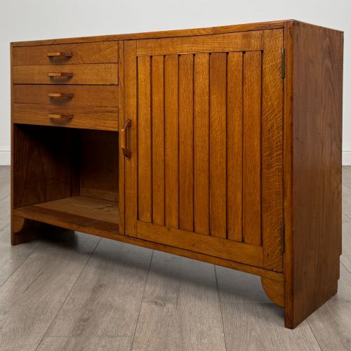 fig 2. A compact golden oak sideboard featuring four shallow drawers on the left, an open shelf below, and a slatted single door cabinet on the right.