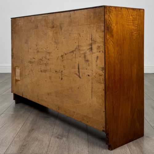 fig 6. A compact golden oak sideboard featuring four shallow drawers on the left, an open shelf below, and a slatted single door cabinet on the right.