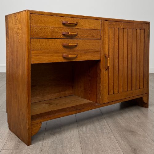 fig 8. A compact golden oak sideboard featuring four shallow drawers on the left, an open shelf below, and a slatted single door cabinet on the right.