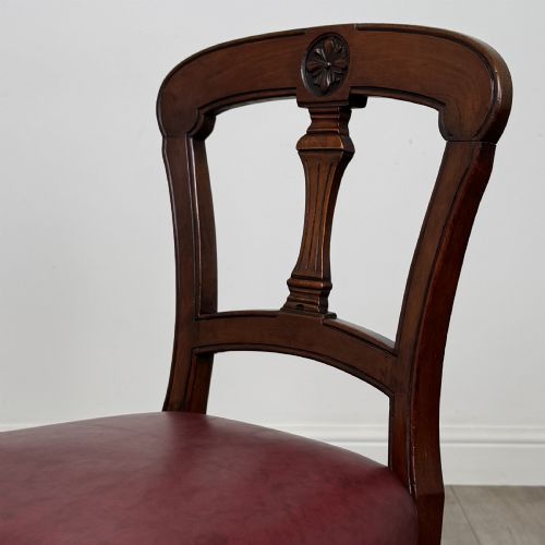 fig 3. A set of four 19th-century mahogany dining chairs featuring carved open backs, dark red leather upholstered seats with stud trim, and turned front legs.