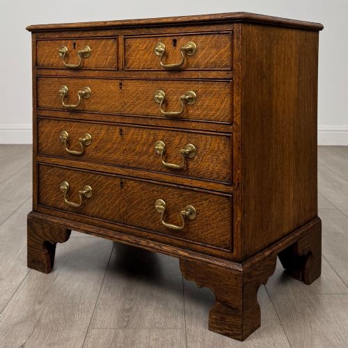 fig 1. An antique oak chest of drawers featuring two short over three long drawers with brass swan-neck handles and shaped bracket feet.