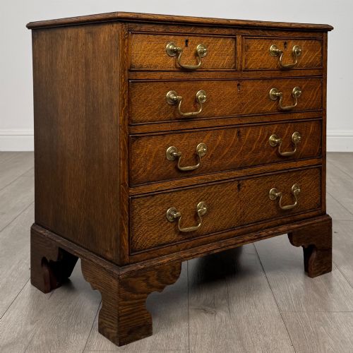 fig 7. An antique oak chest of drawers featuring two short over three long drawers with brass swan-neck handles and shaped bracket feet.