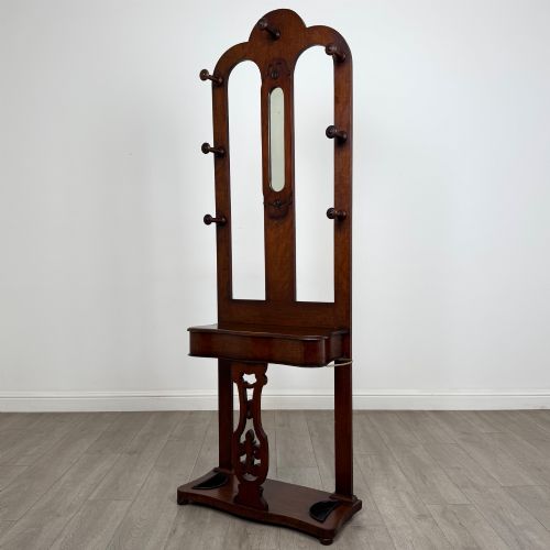 fig 1. A freestanding Victorian mahogany hall stand featuring turned coat pegs, a narrow central mirror panel, a small shelf, and an umbrella holder base.