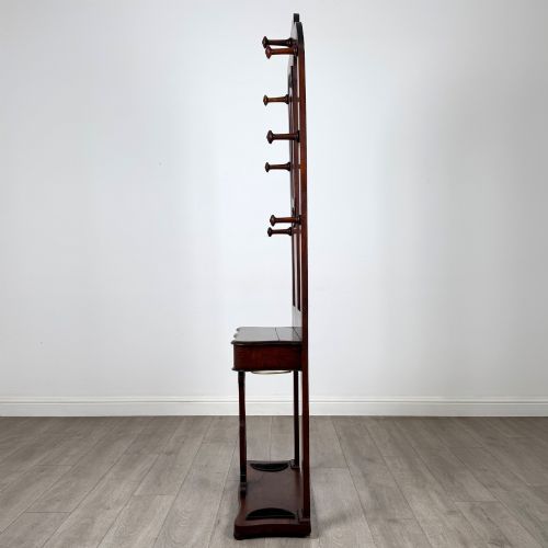fig 2. A freestanding Victorian mahogany hall stand featuring turned coat pegs, a narrow central mirror panel, a small shelf, and an umbrella holder base.
