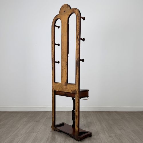 fig 5. A freestanding Victorian mahogany hall stand featuring turned coat pegs, a narrow central mirror panel, a small shelf, and an umbrella holder base.