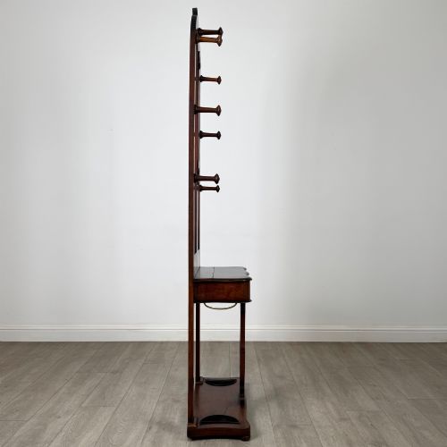 fig 6. A freestanding Victorian mahogany hall stand featuring turned coat pegs, a narrow central mirror panel, a small shelf, and an umbrella holder base.