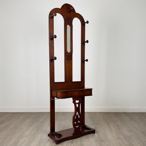 fig 7. A freestanding Victorian mahogany hall stand featuring turned coat pegs, a narrow central mirror panel, a small shelf, and an umbrella holder base.