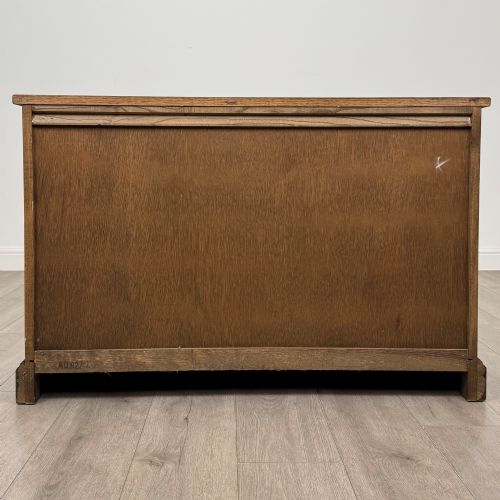 fig 5. A dark oak low cupboard featuring canted corners, carved linenfold door panels, an upper drawer with carved foliage, and brass hinges.
