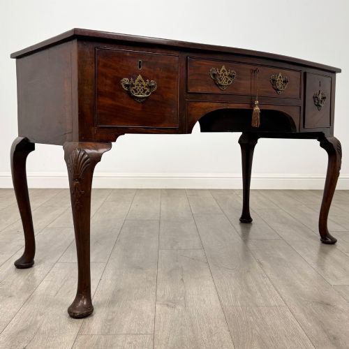fig 7. An Edwardian mahogany writing table with cabriole legs, carved knee detailing, three drawers with ornate brass handles, and a central arched kneehole.
