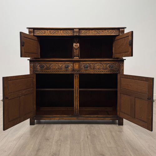 fig 1. A dark carved oak court cupboard featuring two top doors with relief carving, bulbous turned supports, two drawers, and two panelled cupboard doors below.