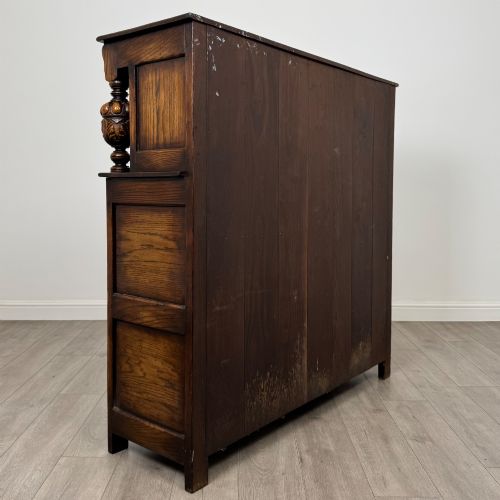 fig 4. A dark carved oak court cupboard featuring two top doors with relief carving, bulbous turned supports, two drawers, and two panelled cupboard doors below.