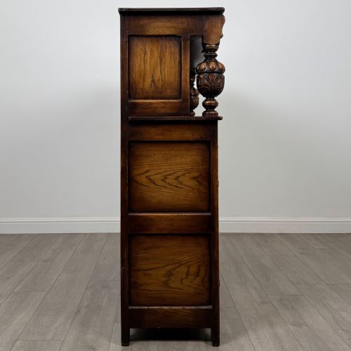 fig 7. A dark carved oak court cupboard featuring two top doors with relief carving, bulbous turned supports, two drawers, and two panelled cupboard doors below.