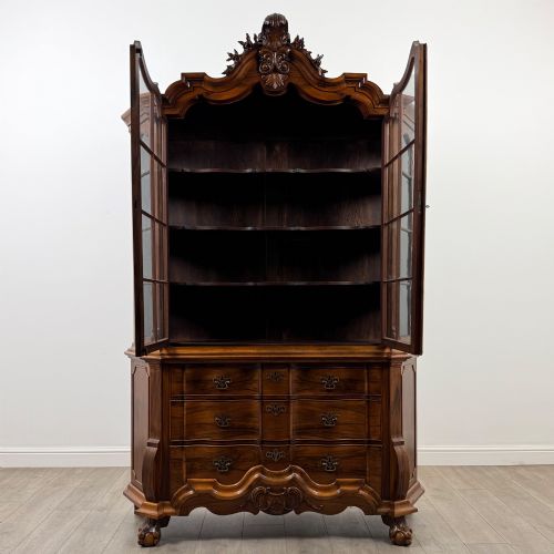 fig 1. A Dutch walnut display cabinet featuring a carved bonnet-top pediment, multi-pane glazed doors, and a lower chest of drawers on carved claw-and-ball feet.