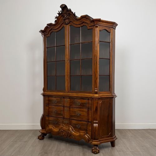 fig 2. A Dutch walnut display cabinet featuring a carved bonnet-top pediment, multi-pane glazed doors, and a lower chest of drawers on carved claw-and-ball feet.