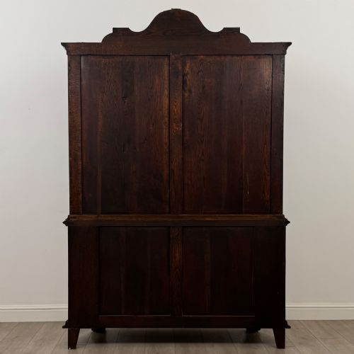 fig 5. A Dutch walnut display cabinet featuring a carved bonnet-top pediment, multi-pane glazed doors, and a lower chest of drawers on carved claw-and-ball feet.