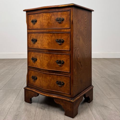 fig 1. A small 20th-century serpentine chest of drawers with four drawers featuring burr walnut veneer, brass drop handles, and bracket feet.