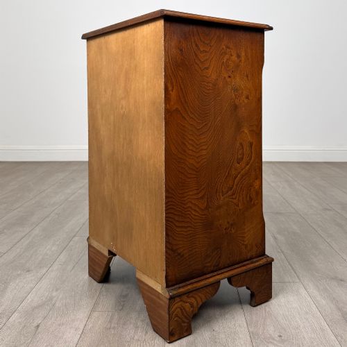 fig 5. A small 20th-century serpentine chest of drawers with four drawers featuring burr walnut veneer, brass drop handles, and bracket feet.