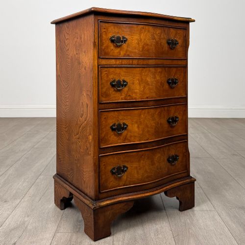 fig 7. A small 20th-century serpentine chest of drawers with four drawers featuring burr walnut veneer, brass drop handles, and bracket feet.