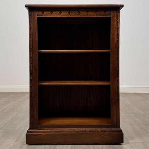 fig 1. A small vintage dark oak bookcase featuring three open shelves, decorative carved detailing along the frieze and side uprights, and a solid plinth base.