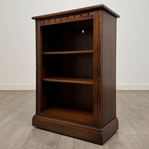 fig 2. A small vintage dark oak bookcase featuring three open shelves, decorative carved detailing along the frieze and side uprights, and a solid plinth base.