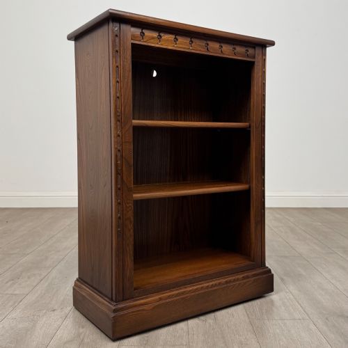fig 8. A small vintage dark oak bookcase featuring three open shelves, decorative carved detailing along the frieze and side uprights, and a solid plinth base.