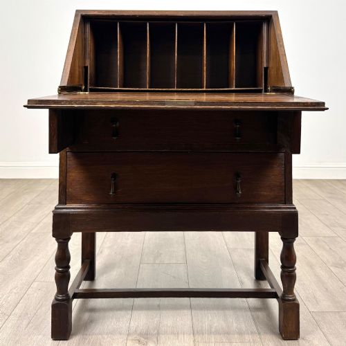 fig 1. An Edwardian dark oak writing bureau featuring a sloped drop-down lid, two lower drawers with teardrop handles, and turned legs connected by stretchers.