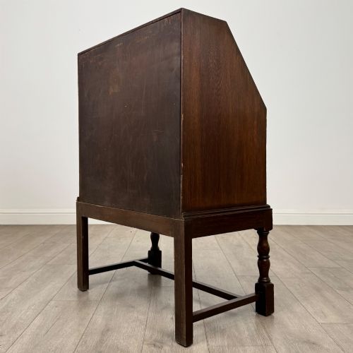 fig 6. An Edwardian dark oak writing bureau featuring a sloped drop-down lid, two lower drawers with teardrop handles, and turned legs connected by stretchers.