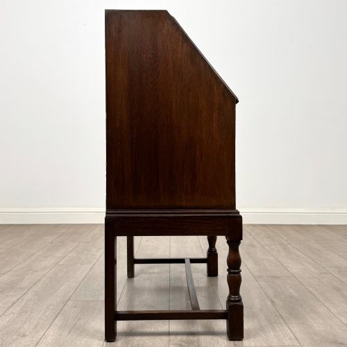 fig 7. An Edwardian dark oak writing bureau featuring a sloped drop-down lid, two lower drawers with teardrop handles, and turned legs connected by stretchers.