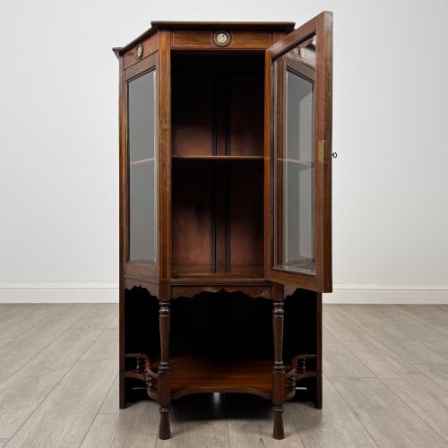 fig 1. An antique walnut display cabinet featuring glazed door and side panels, decorative inlay along the frieze, and an open lower shelf resting on turned front legs.