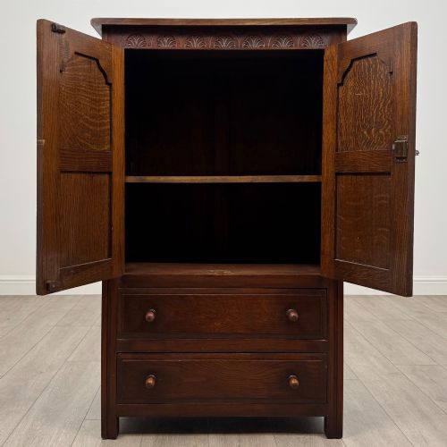 fig 1. A dark oak cabinet featuring carved top frieze detailing, two arched fielded panel doors with exposed iron hinges, and two lower drawers with turned wooden knobs.