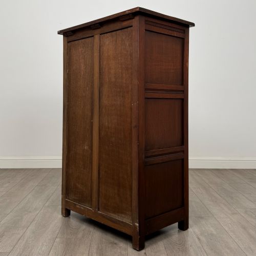 fig 6. A dark oak cabinet featuring carved top frieze detailing, two arched fielded panel doors with exposed iron hinges, and two lower drawers with turned wooden knobs.