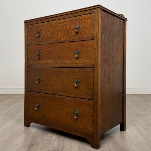 fig 1. Front view of an early 20th-century warm brown oak chest featuring four wide drawers with ornamental brass drop handles.