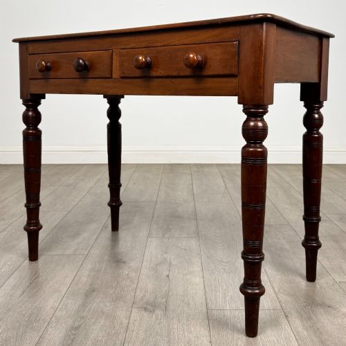 fig 1. A Victorian mahogany writing table featuring two frieze drawers with wooden knobs and turned reeded legs.