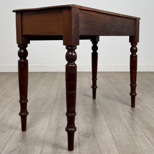 fig 3. A Victorian mahogany writing table featuring two frieze drawers with wooden knobs and turned reeded legs.