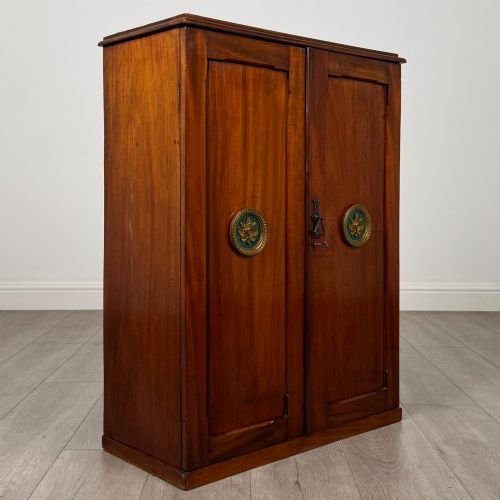 fig 8. A small Victorian mahogany double-door cupboard featuring raised central panels, green circular brass flower mounts, and a decorative central keyhole.