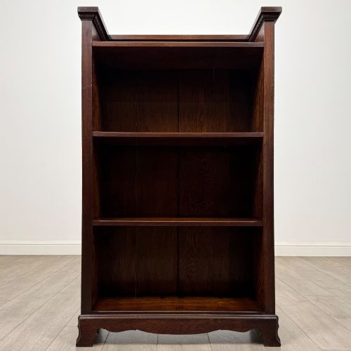 fig 1. An Edwardian open oak bookcase featuring three interior fixed shelves, dark timber finish, carved moulding on top uprights, and a shaped plinth base.
