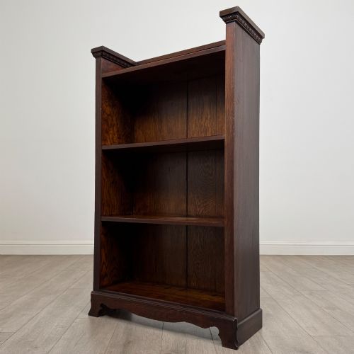 fig 2. An Edwardian open oak bookcase featuring three interior fixed shelves, dark timber finish, carved moulding on top uprights, and a shaped plinth base.