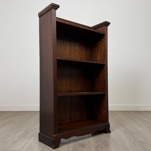 fig 8. An Edwardian open oak bookcase featuring three interior fixed shelves, dark timber finish, carved moulding on top uprights, and a shaped plinth base.