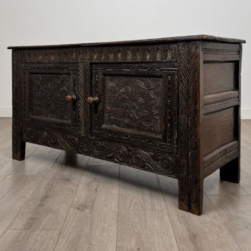 fig 2. A low dark oak Victorian cupboard featuring two doors with relief carvings of birds and flowers, flanked by leafy carved uprights and a carved frieze.