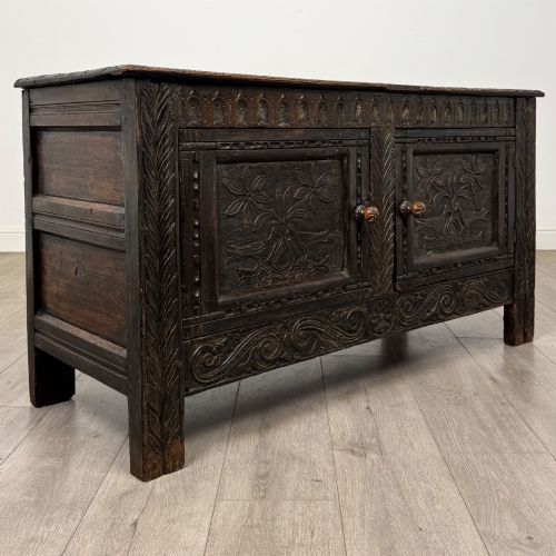 fig 8. A low dark oak Victorian cupboard featuring two doors with relief carvings of birds and flowers, flanked by leafy carved uprights and a carved frieze.