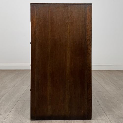 fig 2. A dark oak chest of drawers featuring carved vertical linenfold panels and metallic drop handles.
